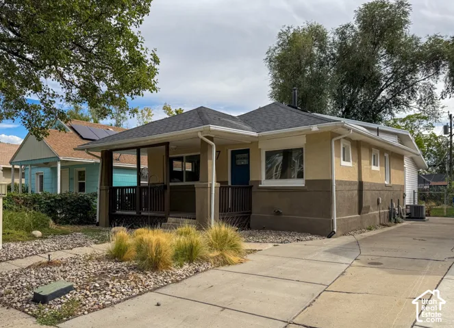 Stucco exterior with a covered front porch, dark asphalt shingle roof, and concrete driveway