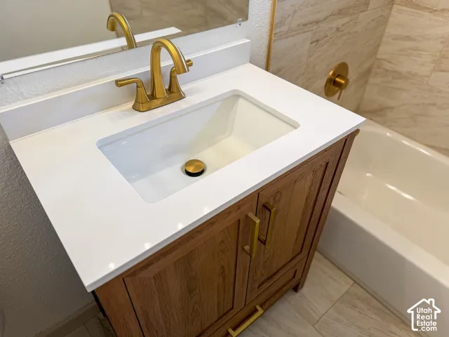 Wood-finish vanity with gold hardware, white countertop with integrated sink, and gold-finish faucet