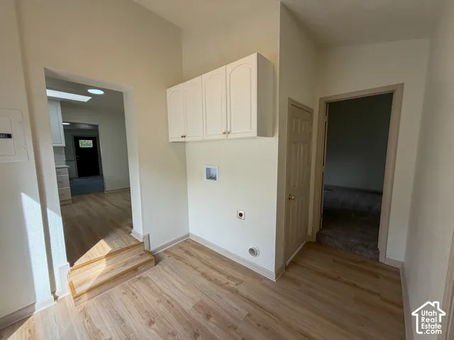 Wood-finish flooring with white baseboards, built-in white cabinetry, and a white interior door with a brass-finish knob