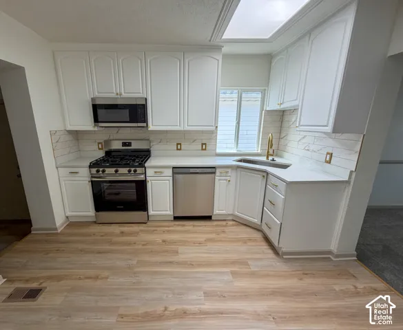 Kitchen featuring white cabinetry, stainless steel appliances, light-toned countertops, a skylight, and wood-finish flooring