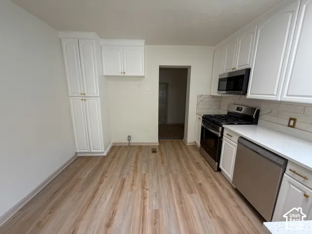 White cabinetry, wood-finish flooring, stainless steel appliances, white countertops, and a white tile backsplash