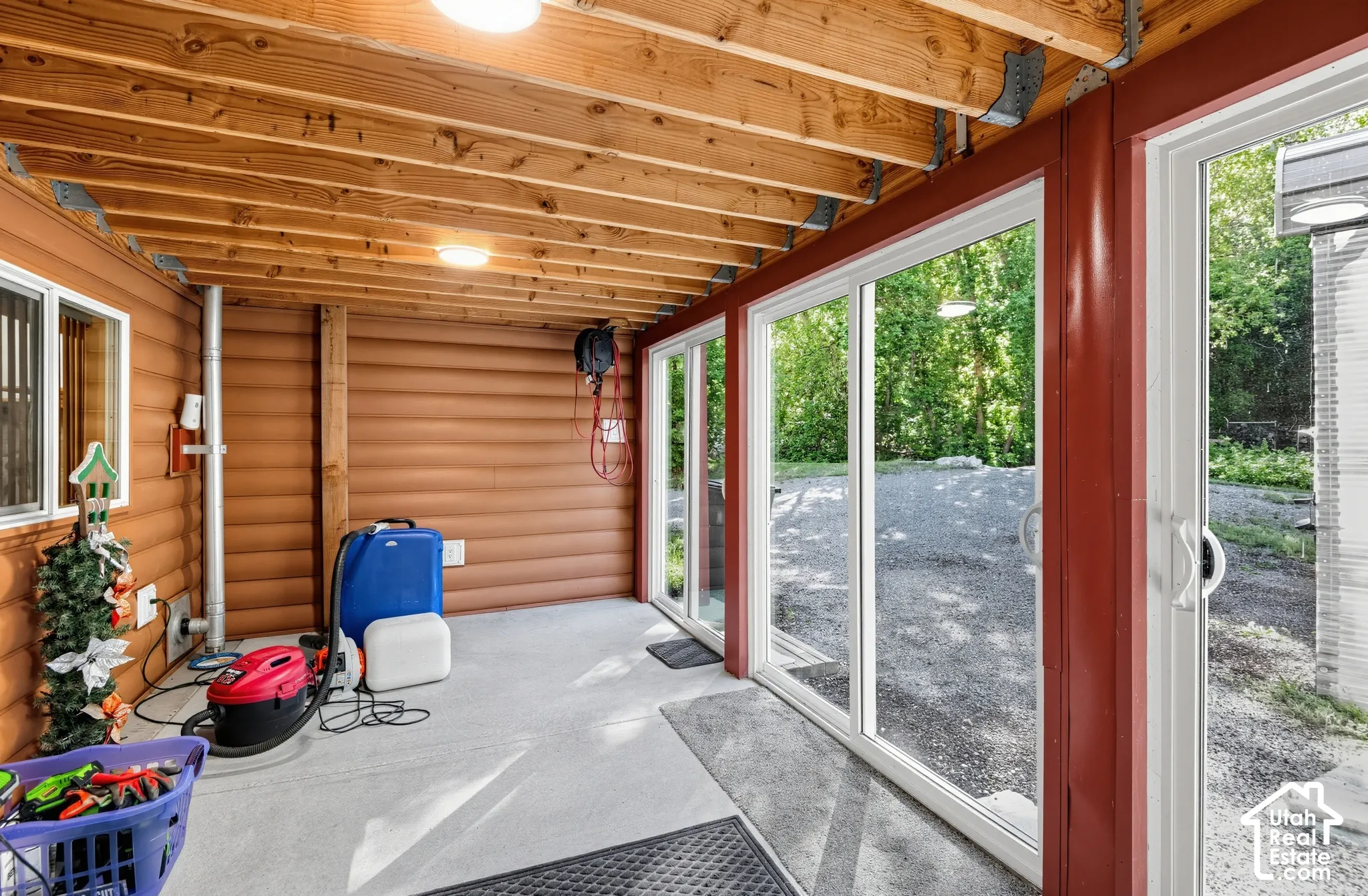 Exposed wood beam ceiling with recessed lighting, wood-paneled walls, multiple sliding glass doors, and durable concrete flooring