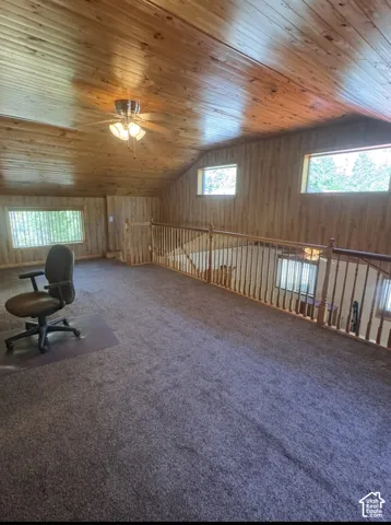 Loft space featuring wood paneling, sloped wood-finish ceiling, ceiling fan, carpeted flooring, and wood-finish railing