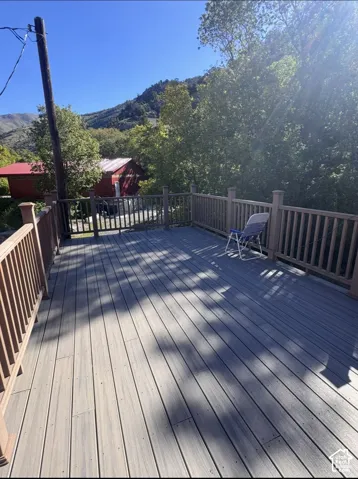 Spacious outdoor deck with composite decking and wood railing, surrounded by mature trees and a distant mountain backdrop