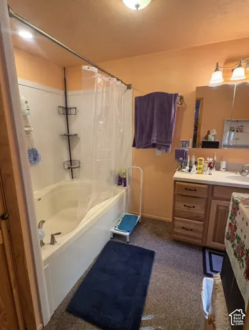 Built-in bathtub with shower, vanity with wood-finish cabinetry, and overhead lighting fixture