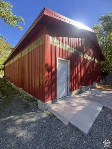 Red metal siding structure with a white entry door, concrete ramp, and gravel ground cover