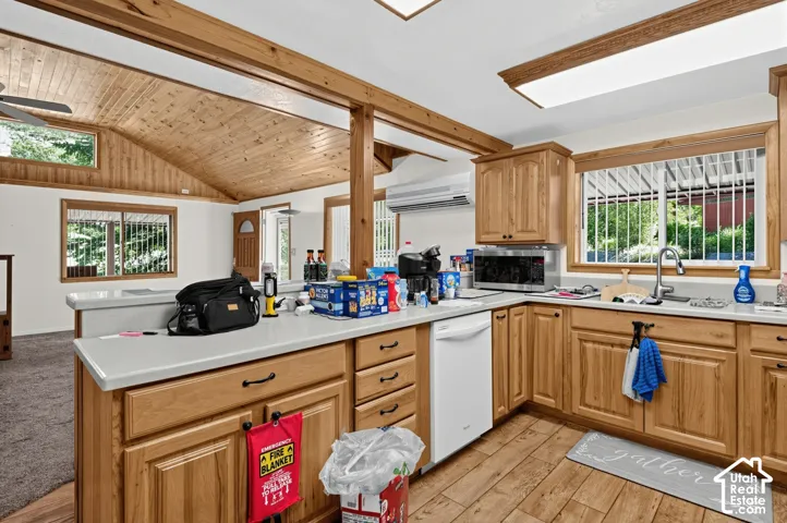 Kitchen featuring wood-finish flooring, wood cabinetry with dark hardware, a corner sink with a gooseneck faucet, and a built-in dishwasher