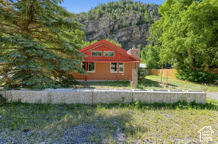 Red roofline accenting the exterior, stone-clad chimney, multiple windows, and a stone-textured retaining wall