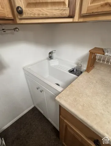 Utility sink with white cabinetry, chrome faucet, and wood-finish upper cabinetry