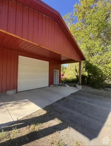 Red metal siding building with a white garage door, concrete pad, covered entry, and gravel driveway