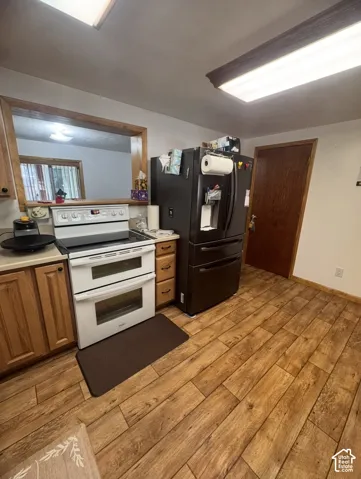 Wood-finish flooring, wood cabinetry, built-in double oven, pass-through window, and a dark-finish refrigerator