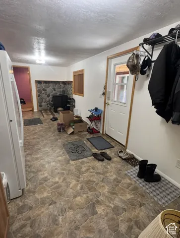 Stone-look flooring with a white entry door, wood-trimmed windows, and a stone-clad fireplace