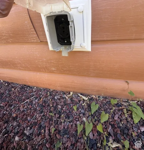 Exterior outlet with protective cover, situated against a wood-finish siding and a ground cover of dark gravel