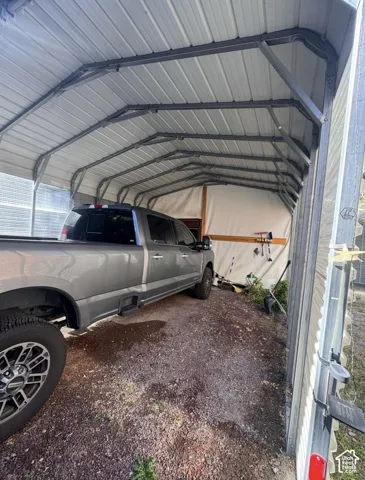Metal carport structure with a corrugated roof paneling and an aggregate surface
