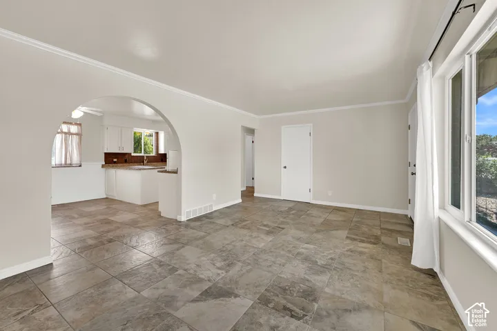 Spacious open-concept living area showcasing tile flooring, abundant natural light from multiple windows, arched architectural detailing, and seamless sightlines to the kitchen with built-in cabinetry and countertop workspace