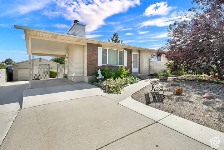 Brick and siding exterior with a covered carport, mature landscaping, and a concrete driveway