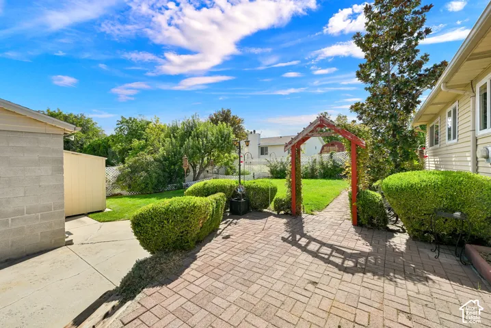 Expansive backyard with a red wood arbor, manicured lawn, paved brick patio, and mature landscaping