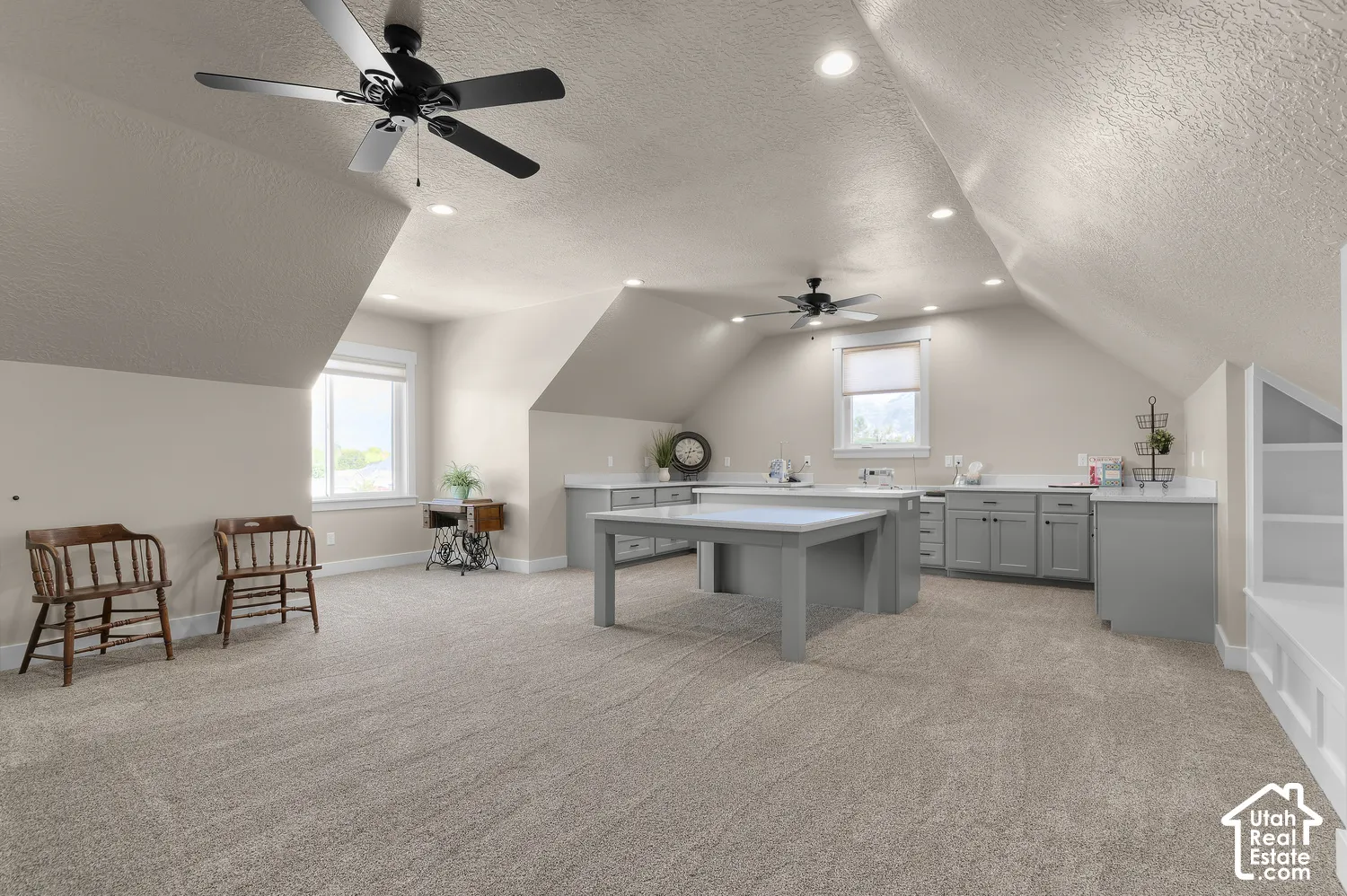 Expansive room featuring sloped ceilings, recessed lighting, two ceiling fans, built-in cabinetry with countertops, and a central built-in island