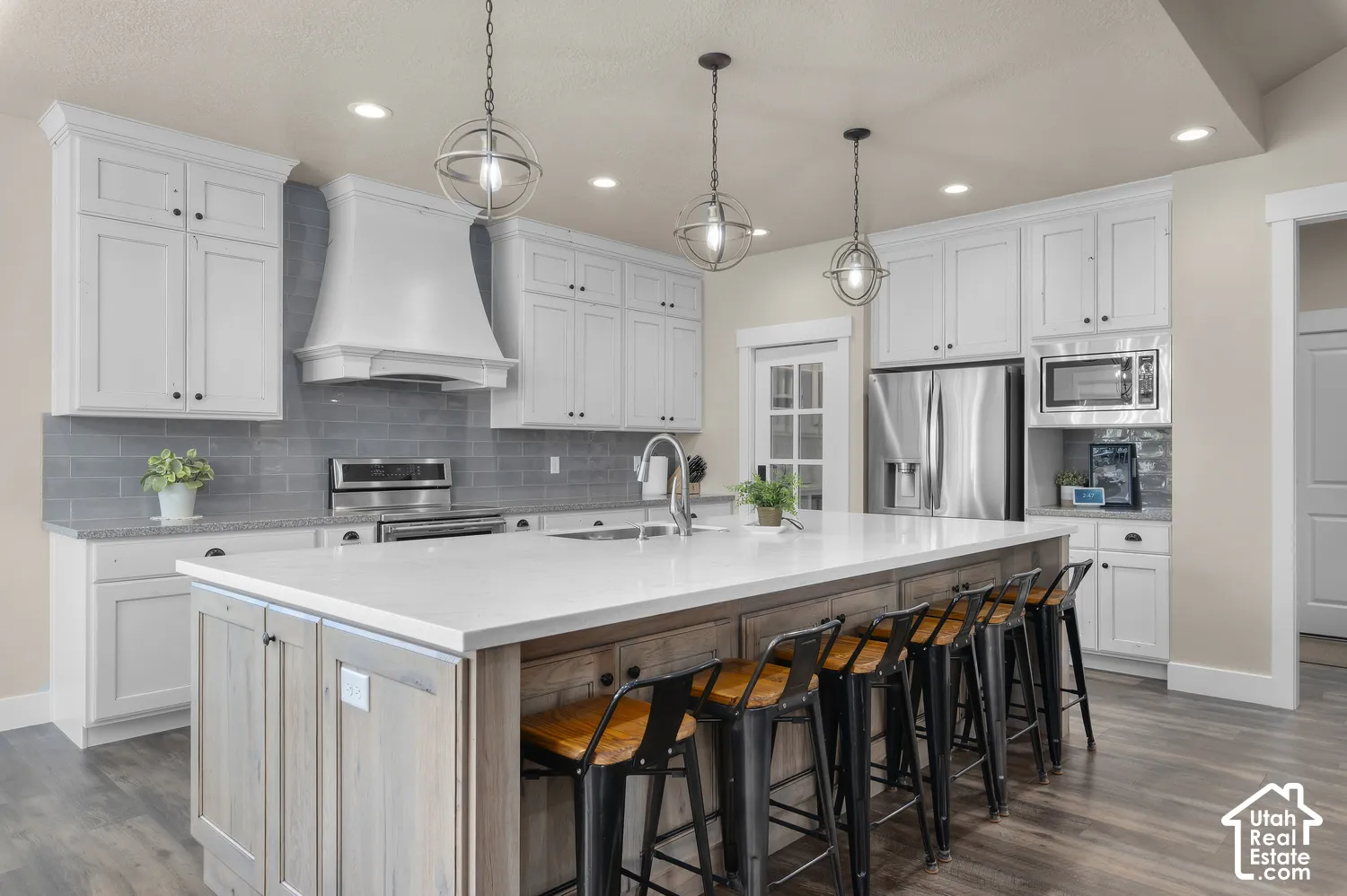 White cabinetry, stainless steel appliances, large kitchen island with seating, pendant lighting, and wood-finish flooring