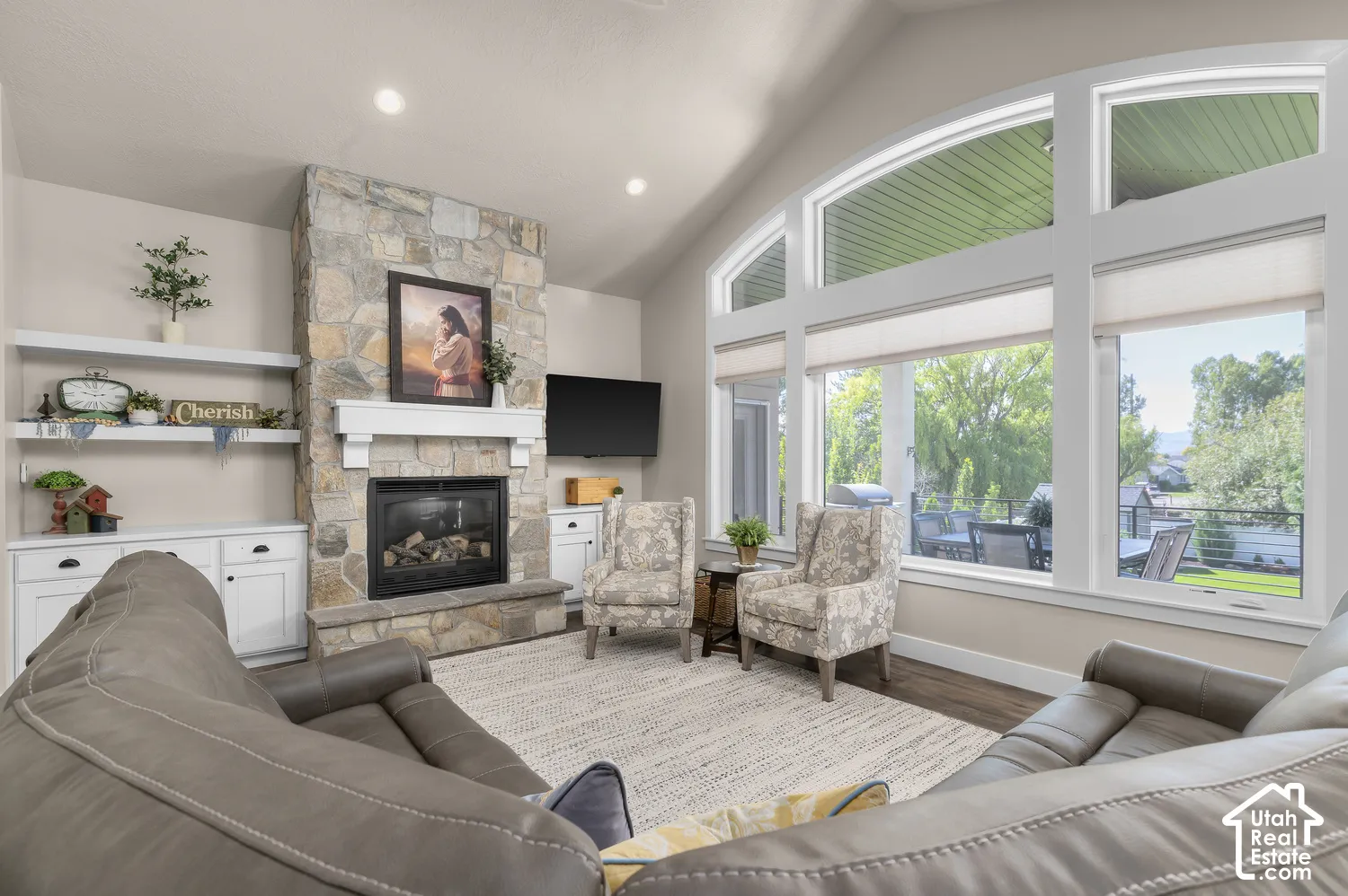 Stone-clad fireplace with a white mantel, built-in shelving, vaulted ceiling, recessed lighting, and large picture windows