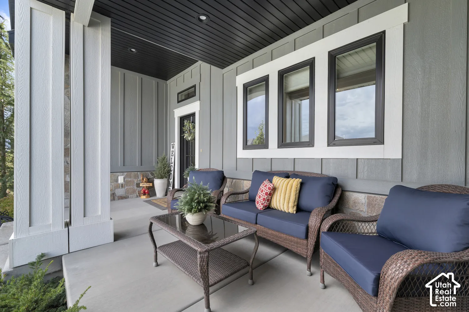 Covered concrete porch with board and batten siding, stone wainscoting, and large windows with dark trim