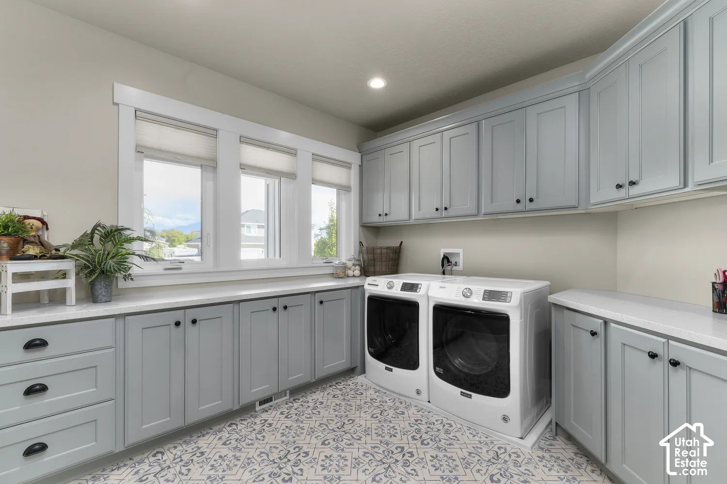 Light-filled utility space featuring a trio of windows, extensive light blue cabinetry, white countertops, and patterned floor tiling