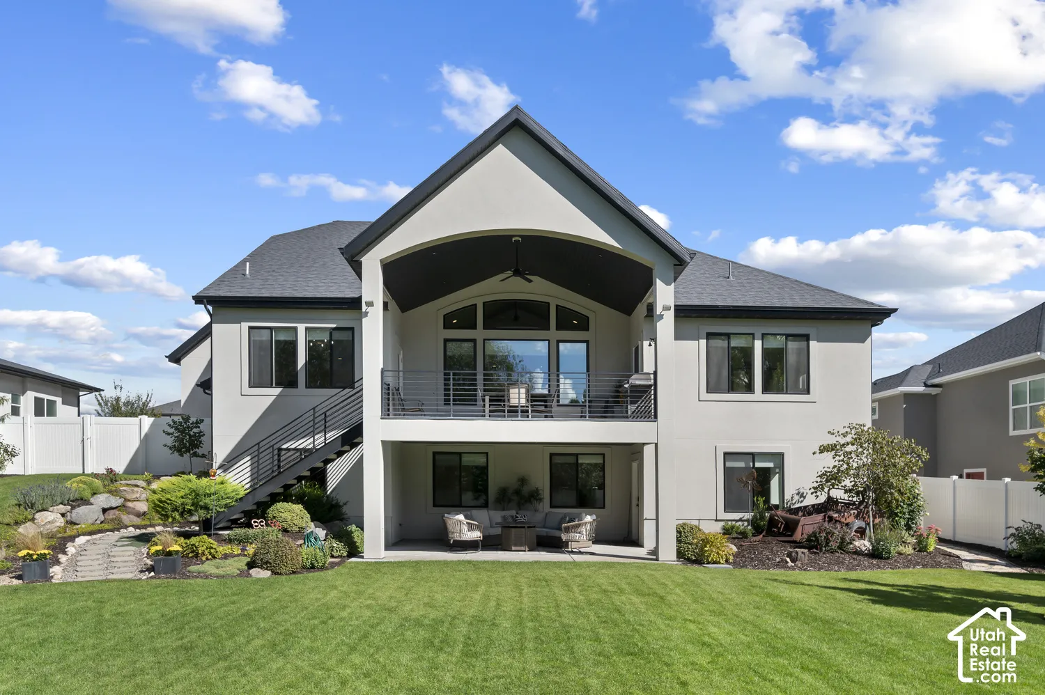 Expansive stucco exterior with multiple windows, a covered upper-level balcony with a railing, and a ground-level covered patio