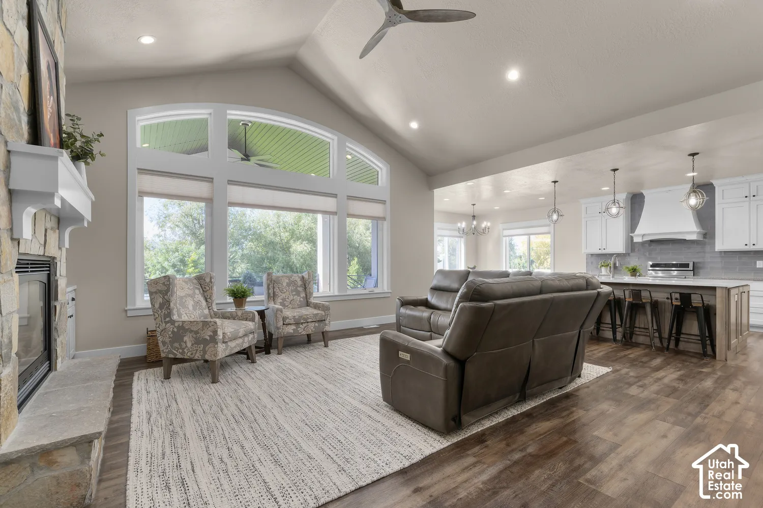 Vaulted ceiling, stone-clad fireplace with mantel, large arched windows, wood-finish flooring, and recessed lighting