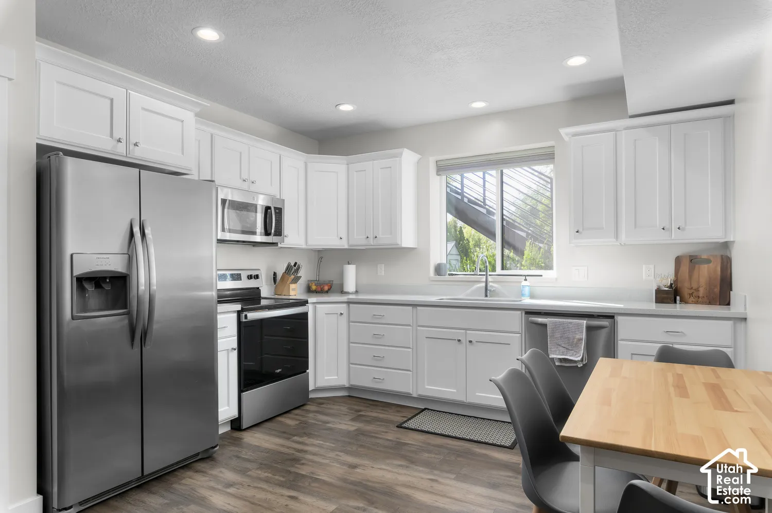 White shaker cabinetry, stainless steel appliances, wood-finish flooring, recessed lighting, and a window with a roller shade; ADU