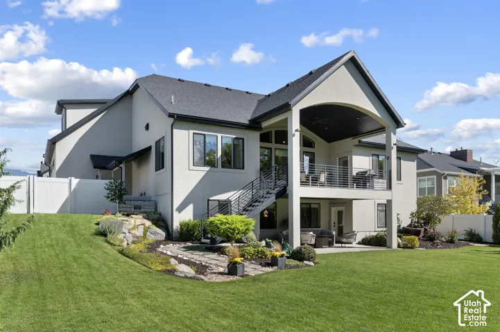 Expansive backyard with a manicured lawn, multi-level stucco exterior, upper-level covered patio with metal railings, and a lower-level patio