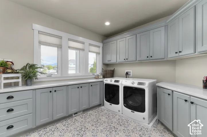 Light-filled utility space featuring a trio of windows, extensive light blue cabinetry, white countertops, and patterned floor tiling