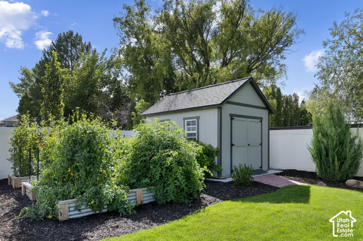 Manicured lawn with raised garden beds, a storage shed with a shingled roof, a brick pathway, and mature landscaping
