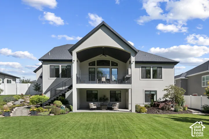 Expansive stucco exterior with multiple windows, a covered upper-level balcony with a railing, and a ground-level covered patio