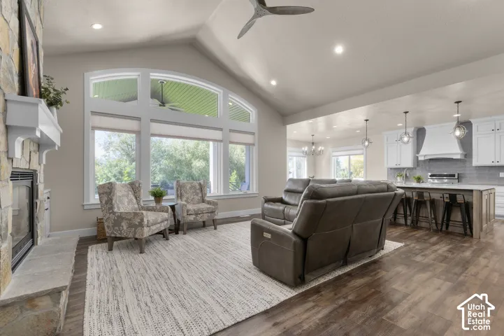 Vaulted ceiling, stone-clad fireplace with mantel, large arched windows, wood-finish flooring, and recessed lighting