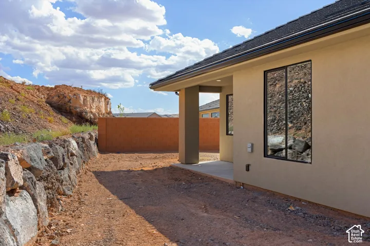 Stucco exterior with black-framed windows, a covered patio, and a stone retaining wall