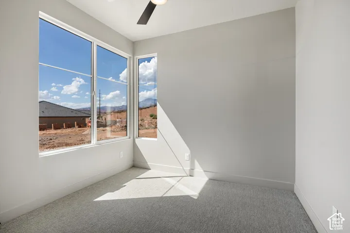 Expansive windows, ceiling fan, neutral wall tones, and carpeted flooring