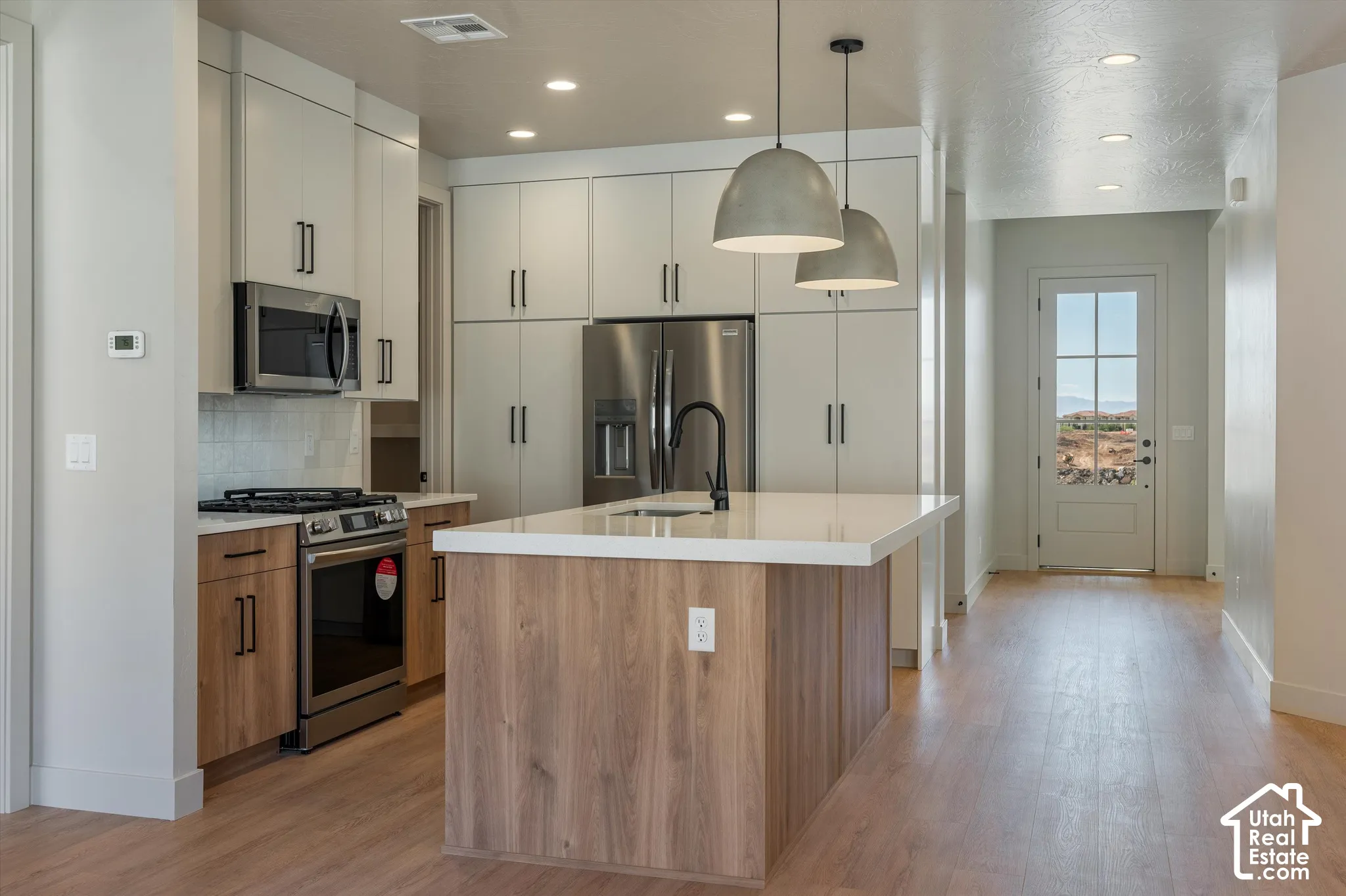 Kitchen featuring wood-finish flooring, two-tone cabinetry, stainless steel appliances, a center island with sink, and recessed lighting