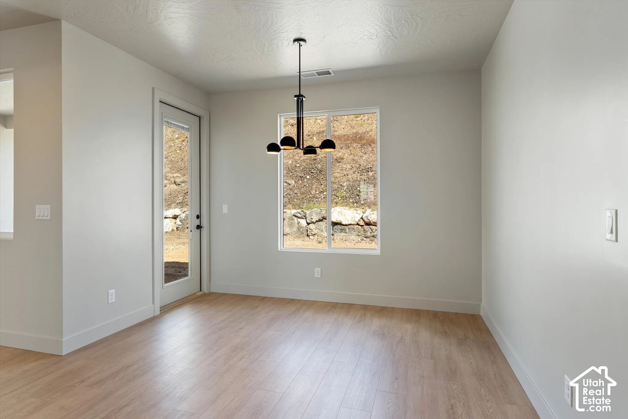 Light-toned wood-finish flooring, white walls, black contemporary chandelier, large window, and a full-light exterior door