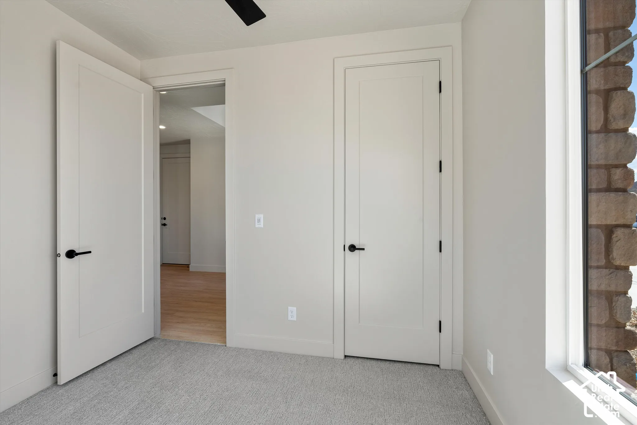 Plush carpet flooring, stone exterior window surround, white interior doors with black hardware, and an overhead ceiling fan