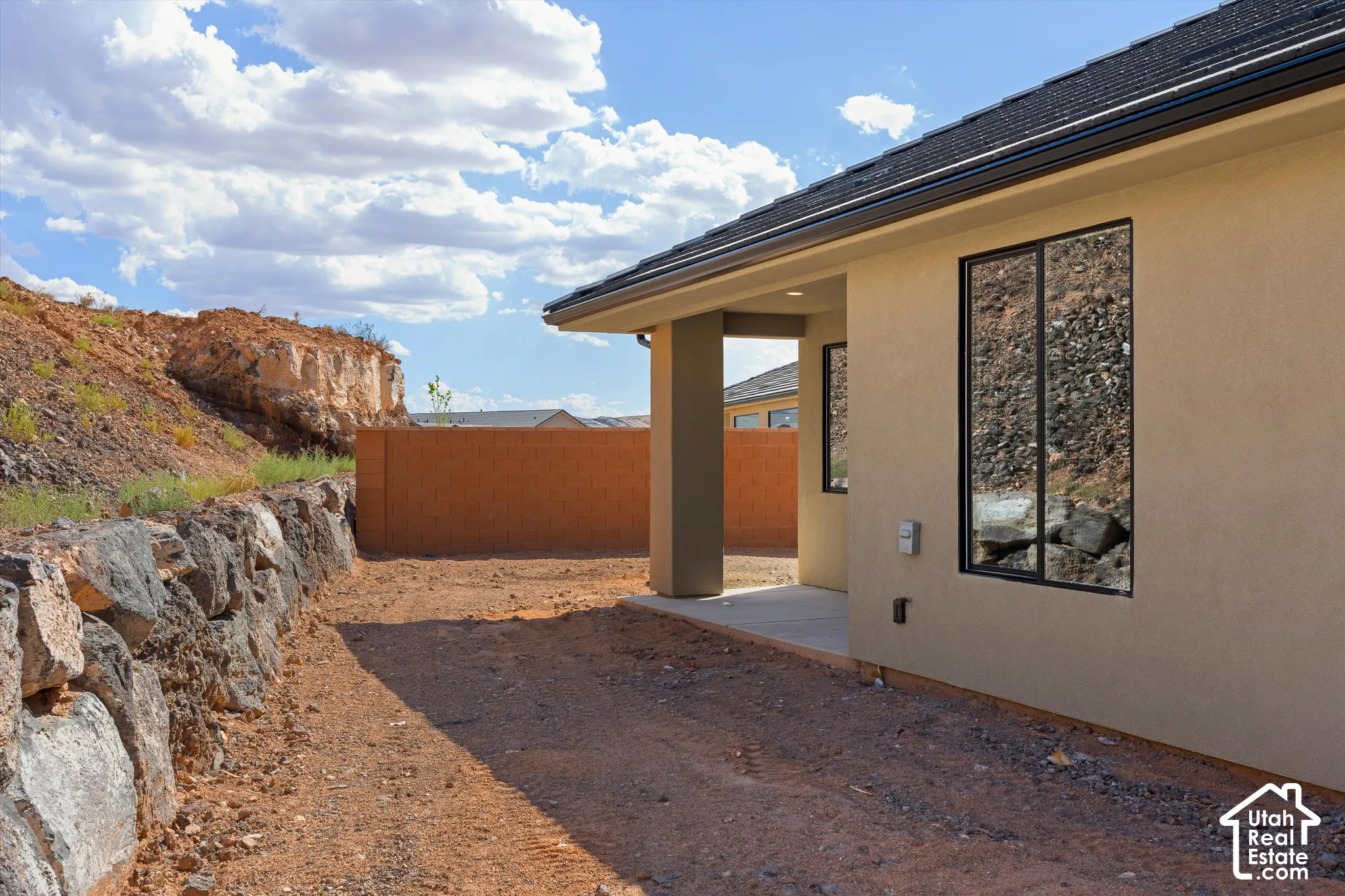 Stucco exterior with black-framed windows, a covered patio, and a stone retaining wall