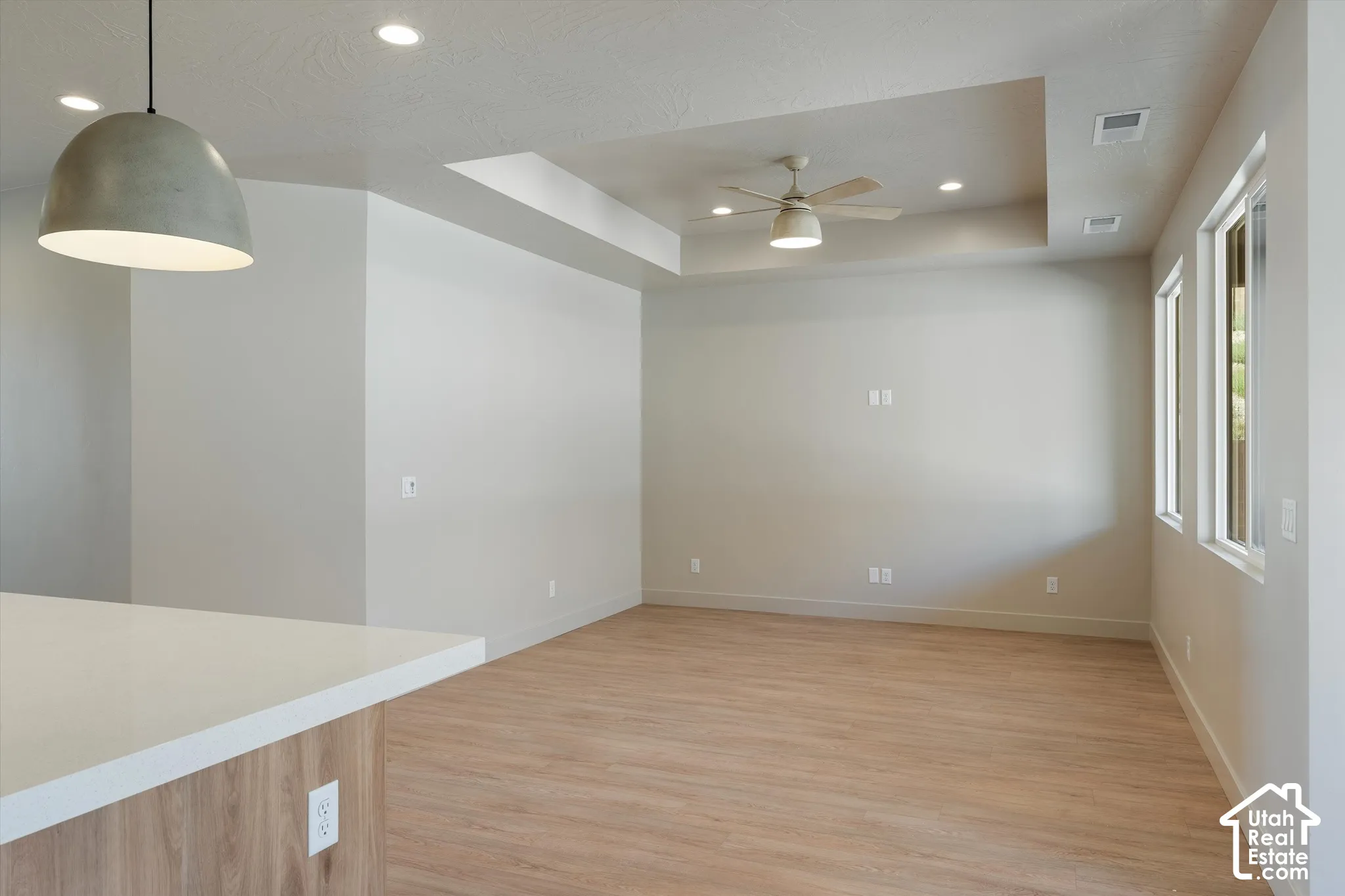 Tray ceiling with recessed lighting and a ceiling fan, wood-finish flooring, and multiple windows