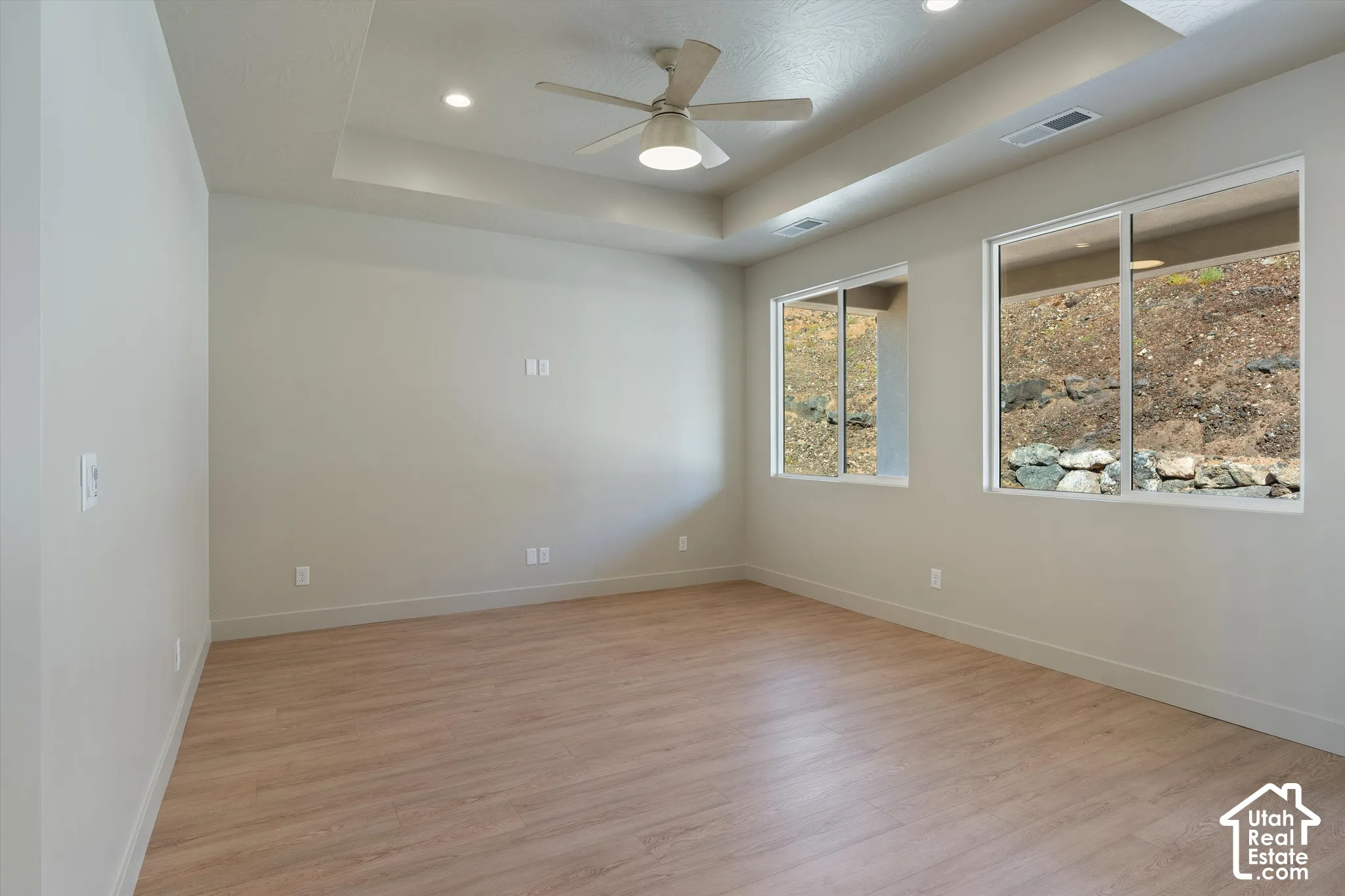 Tray ceiling with recessed lighting, ceiling fan, wood-finish flooring, and multiple windows