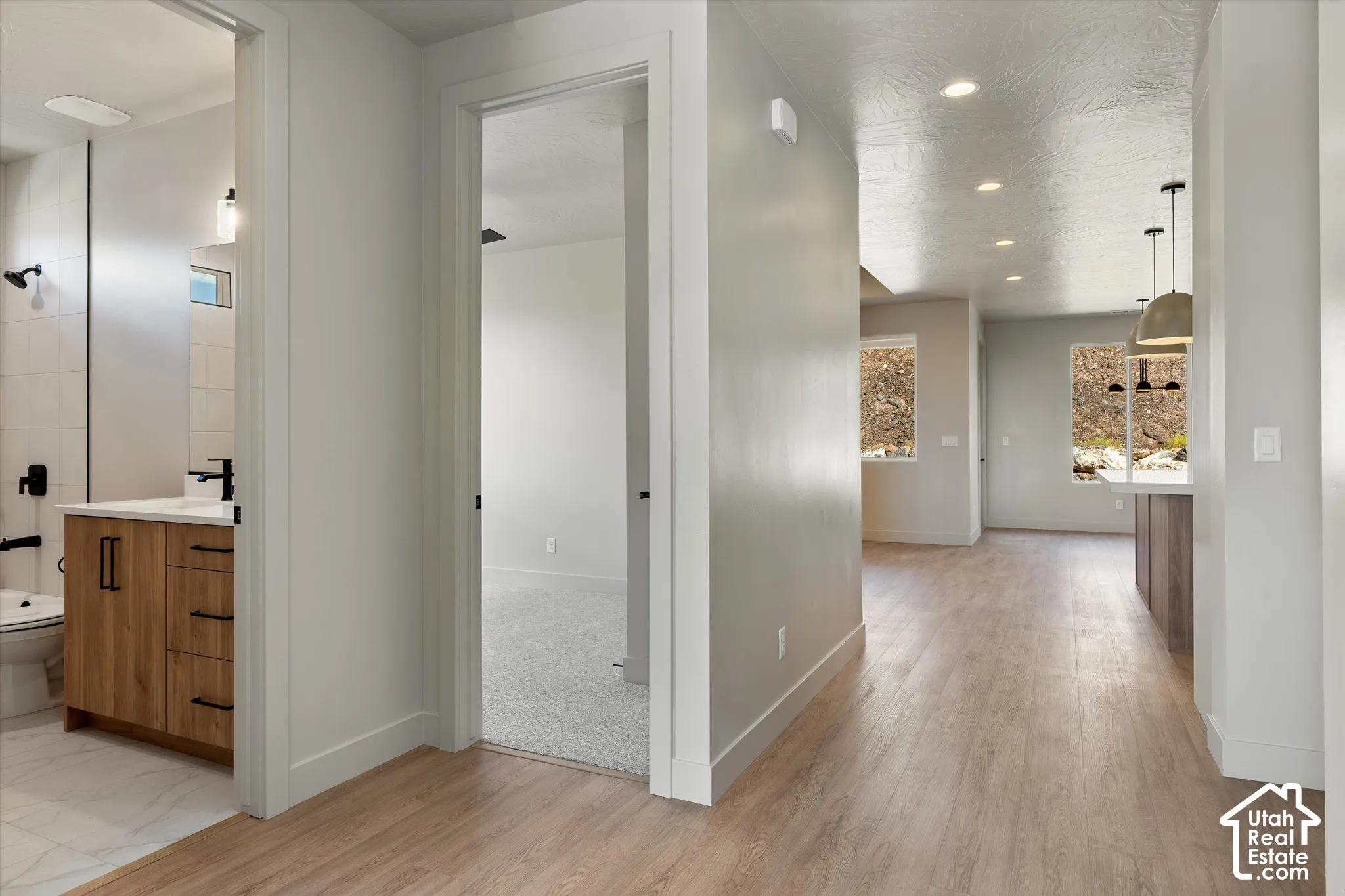 Wood-finish flooring throughout the main corridor, recessed lighting, and a kitchen island with pendant lighting