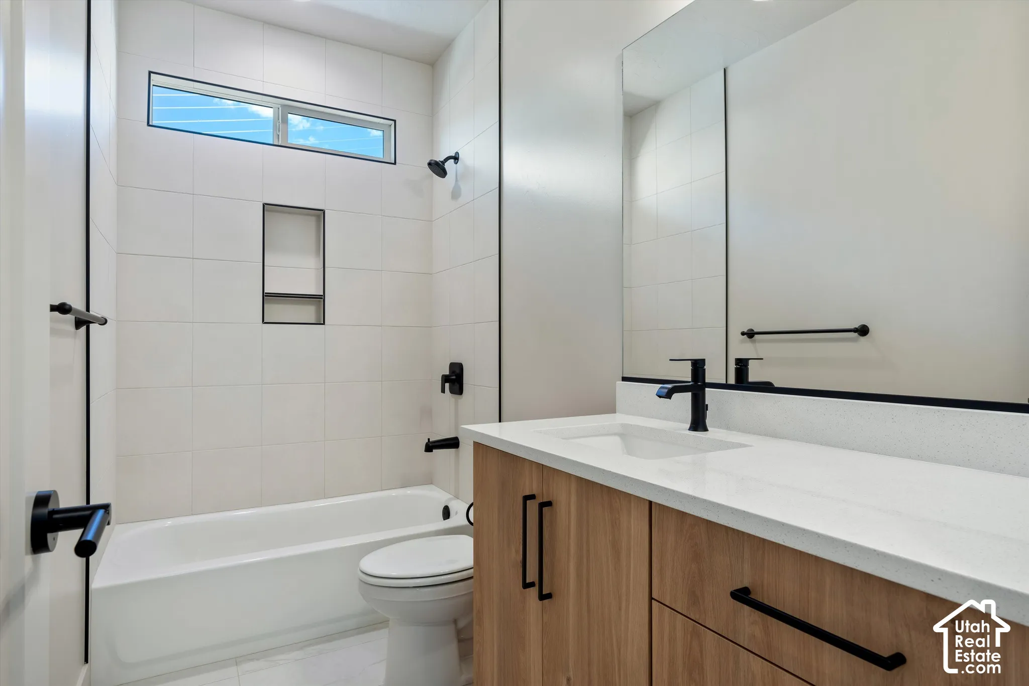 Bathroom featuring a white bathtub, wall-mounted showerhead, built-in shower niche, wood-finish vanity with a single sink, and a large mirror