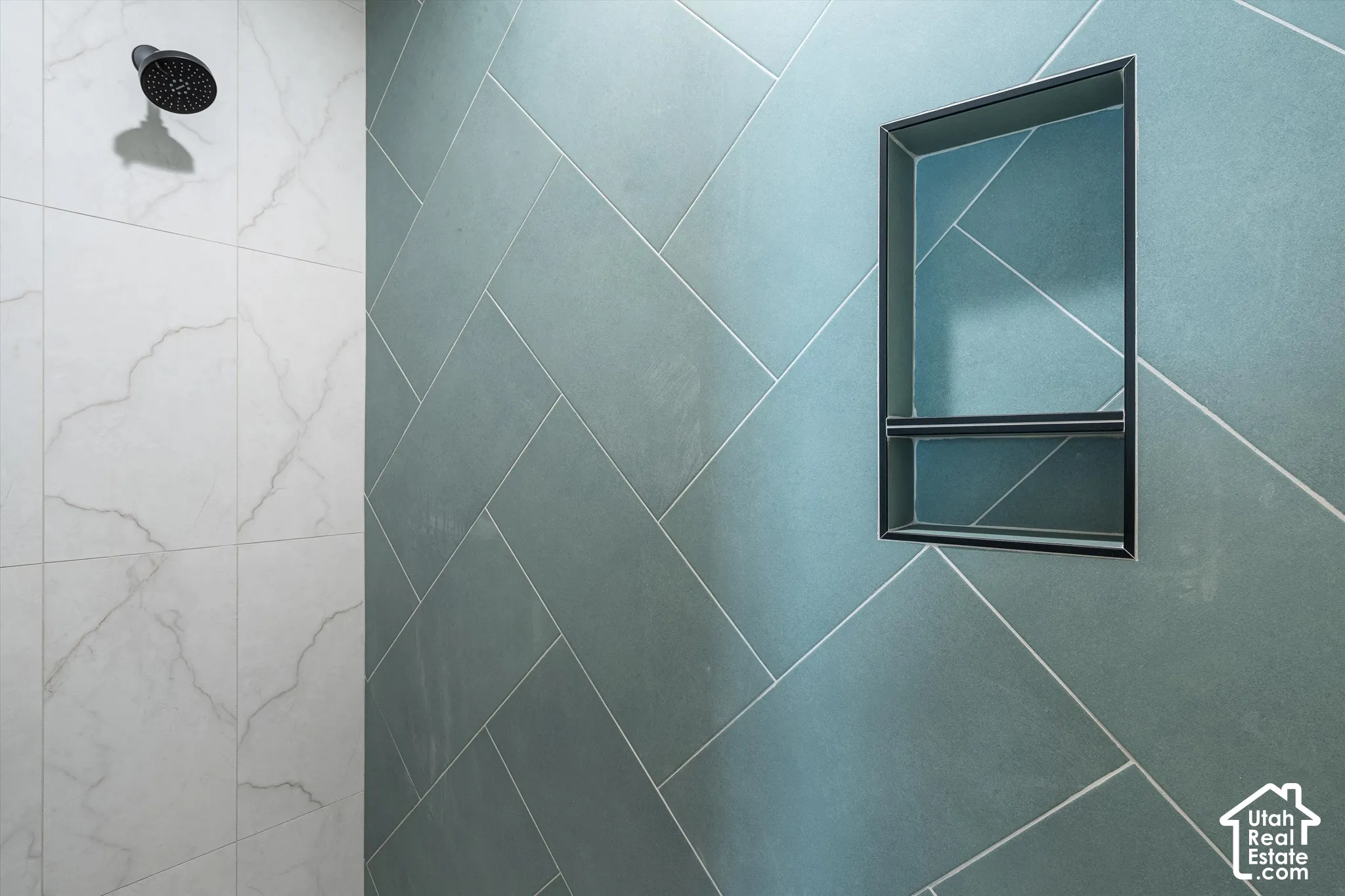 Shower with a matte black showerhead, a built-in recess, and large-format tile with a herringbone pattern