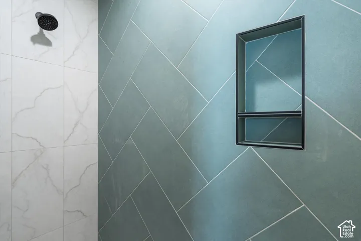Shower with a matte black showerhead, a built-in recess, and large-format tile with a herringbone pattern