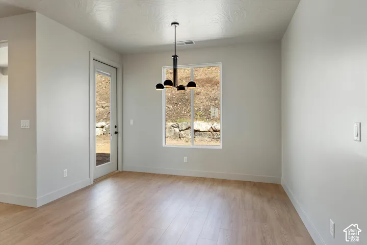 Light-toned wood-finish flooring, white walls, black contemporary chandelier, large window, and a full-light exterior door
