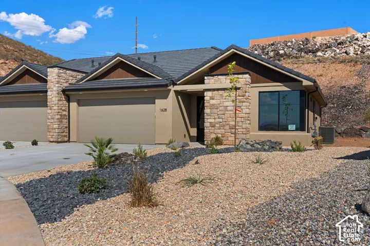 Stone and stucco exterior with dark tile roofing, an integrated garage, and low-maintenance xeriscape landscaping