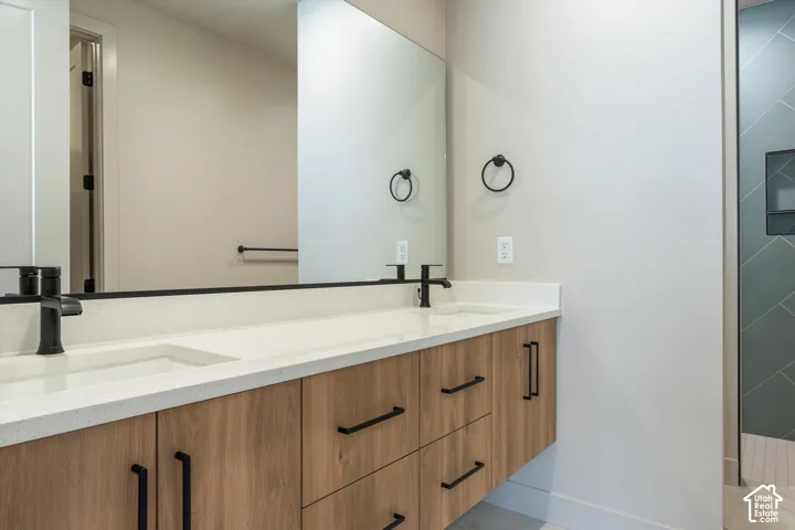 Floating wood-finish vanity with dual integrated sinks, matte black fixtures, full-width mirror, and a walk-in shower featuring patterned tile