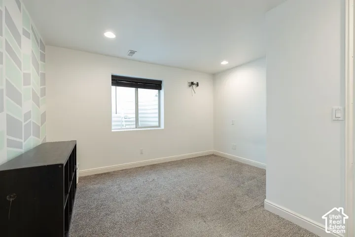 Carpeted room featuring a window with blinds, recessed lighting, and a decorative accent wall